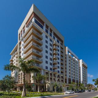 A modern high-rise apartment building with palm trees lining the street.