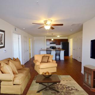 A spacious living room with an open floor plan leading to the kitchen, featuring a ceiling fan, comfortable seating, and hardwood floors.