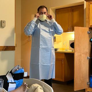 A healthcare worker prepares for a medical procedure, wearing a mask and surgical gown.