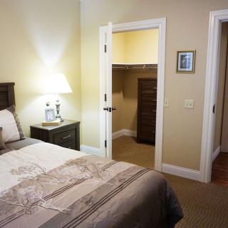A cozy bedroom with a neatly made bed, bedside lamp, and an open closet door.