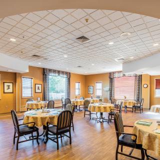 A well-lit dining room with neatly arranged tables and chairs, featuring large windows and decorative elements.