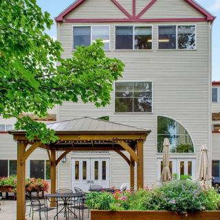 A cozy outdoor seating area with a gazebo in front of a multi-story building surrounded by lush greenery.