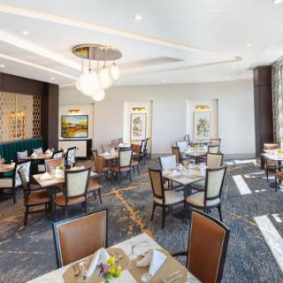 An elegantly designed dining room with neatly arranged tables and chairs, featuring modern chandeliers and decorative artwork on the walls.