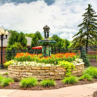 A beautifully landscaped garden with a stone wall and fountain centerpiece, surrounded by vibrant flowers and lush greenery.