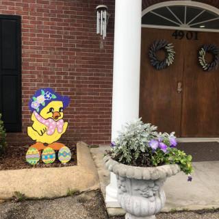 A festive Easter chick decoration adorns the front porch, accompanied by a flower pot and door wreaths.