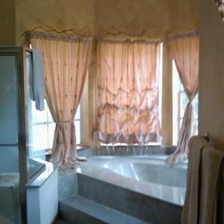A bathroom featuring a large bathtub surrounded by windows with sheer curtains.