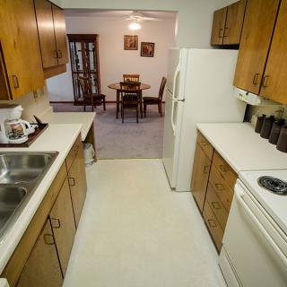 A cozy kitchen leading into a dining area with wooden cabinetry and appliances.