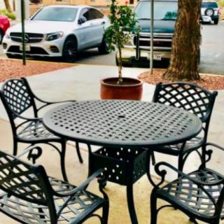 An outdoor patio set with a round table and four chairs near a parking lot, accompanied by a potted plant.