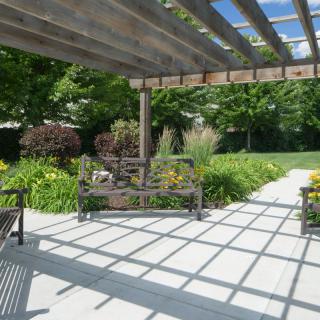 A peaceful garden setting featuring a pergola with benches and lush greenery.