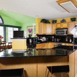A modern kitchen with black countertops, wooden cabinets, and stainless steel appliances, featuring bright green and yellow walls.