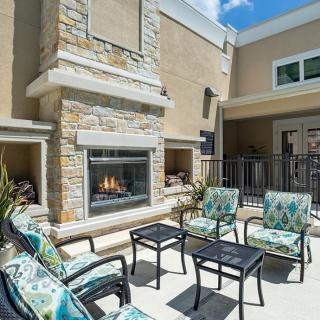 An outdoor patio area featuring a stone fireplace, comfortable seating, and tables under a clear blue sky.