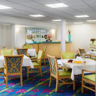A well-lit dining area with neatly arranged tables and chairs, featuring colorful carpet and decor.