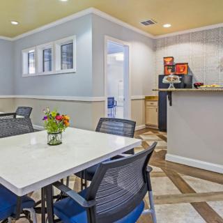 A modern dining area with a white table, black mesh chairs, and a small beverage station in the corner.