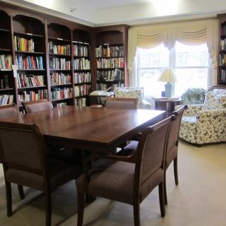 A cozy library room with bookshelves, a large table, and comfortable chairs.