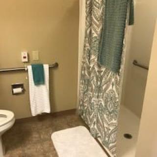 A bathroom featuring a toilet, a shower with a patterned curtain, and neatly hung towels.