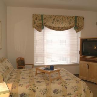 A cozy bedroom with floral decor, featuring a bed, a television, and a window with curtains.