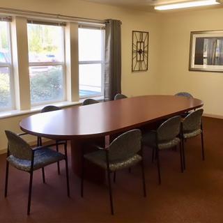 A conference room with a large oval table and several chairs, featuring natural light from the windows.