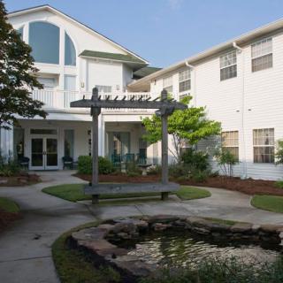 A peaceful courtyard garden with a pond and a pergola in front of a residential building.