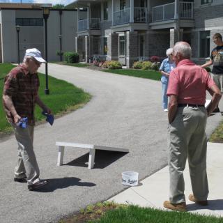 A group of seniors enjoying a game of cornhole outdoors on a sunny day.