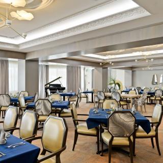 An elegant dining room with neatly arranged tables and chairs, featuring a grand piano.