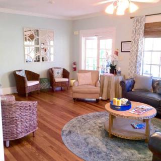 A cozy living room featuring a round rug, wicker chairs, and abundant natural light.