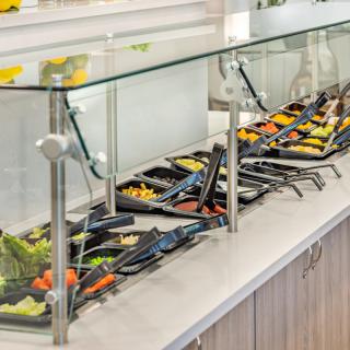 A self-service salad bar with a variety of fresh vegetables in a restaurant setting.