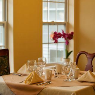 An elegantly set dining table with glasses, napkins, and a flower centerpiece by the window.