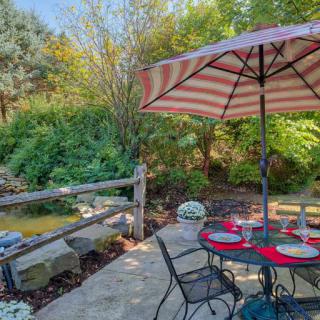 A cozy patio with a striped umbrella, set for dining amidst lush garden scenery.
