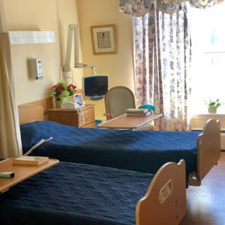 A serene hospital room featuring two patient beds, adorned with blue bedding, and bathed in natural light.