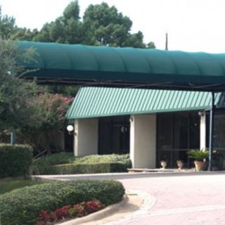 A building entrance featuring a green canopy and landscaped surroundings.