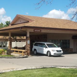 A welcoming entrance to a commercial building with a white van parked outside under a partially cloudy sky.