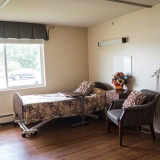 An empty hospital room with a bed, chairs, and a window.