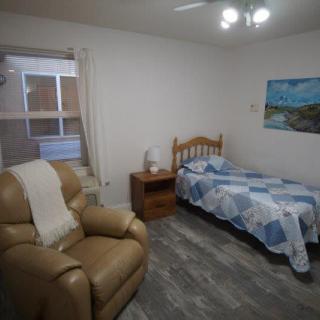 A cozy bedroom with a single bed, armchair, and a painting on the wall.