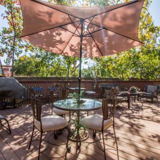 A sunny outdoor patio with a table, chairs, and an umbrella on a wooden deck.
