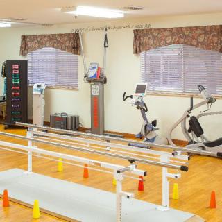 A rehabilitation room with exercise equipment including parallel bars and stationary bikes.