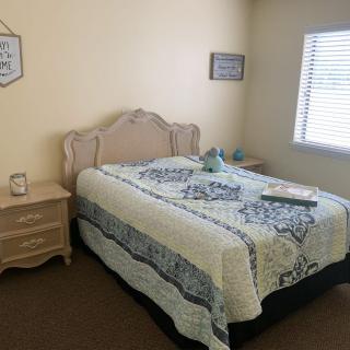 A cozy bedroom with a neatly made bed and two nightstands, featuring a window with blinds.