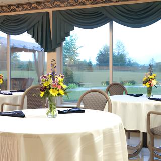 A beautifully set dining room with round tables, decorated with floral centerpieces, overlooking a scenic outdoor view.