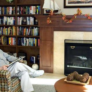 A person reading in a cozy living room with a fireplace and a bookshelf.