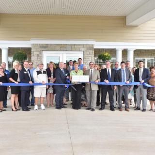 A group of people participating in a ribbon-cutting ceremony outside a building.