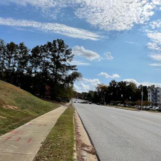 A quiet road lined with trees and a sidewalk under a partly cloudy sky.