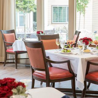 A well-set dining area with tables and chairs, adorned with flowers, ready for guests.
