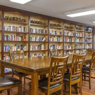A quiet library reading room with wooden tables and chairs surrounded by bookshelves filled with books.