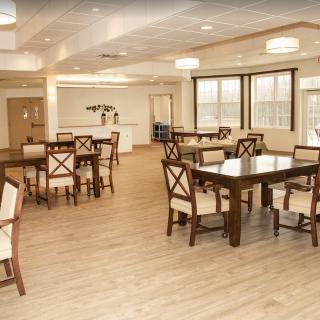 A spacious dining area with wooden tables and chairs set on a light wood floor, illuminated by ceiling lights.