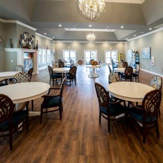 A spacious dining room with elegant chandeliers and wooden floors, featuring several round tables and chairs.
