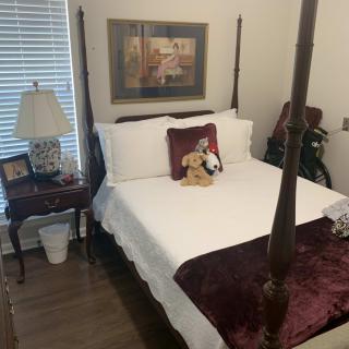A cozy bedroom featuring a four-poster bed with decorative pillows, a nightstand with a lamp, and a painting on the wall.