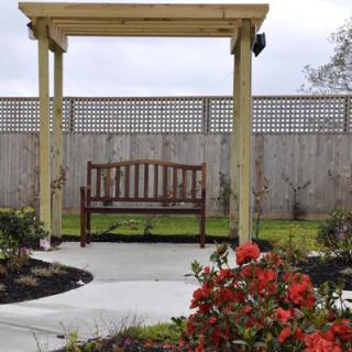 A serene garden scene with a wooden bench under a pergola, surrounded by colorful flowers.