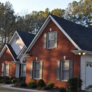 A brick house in a suburban neighborhood shaded by nearby trees.
