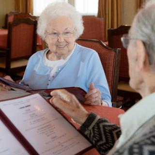Two elderly individuals are sitting at a restaurant table, reviewing the menu together.