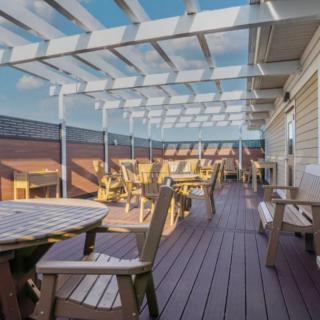 A spacious outdoor patio with wooden furniture and a pergola under a sunny sky.