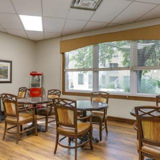 A cozy dining area with tables and chairs, featuring a large window and wooden flooring.